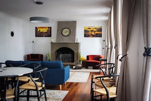 A living room with a fireplace, blue sofas, and a dining area with chairs and a table. - Aurora Hostel - Suítes e Dormitórios  (Angra do Heroísmo)