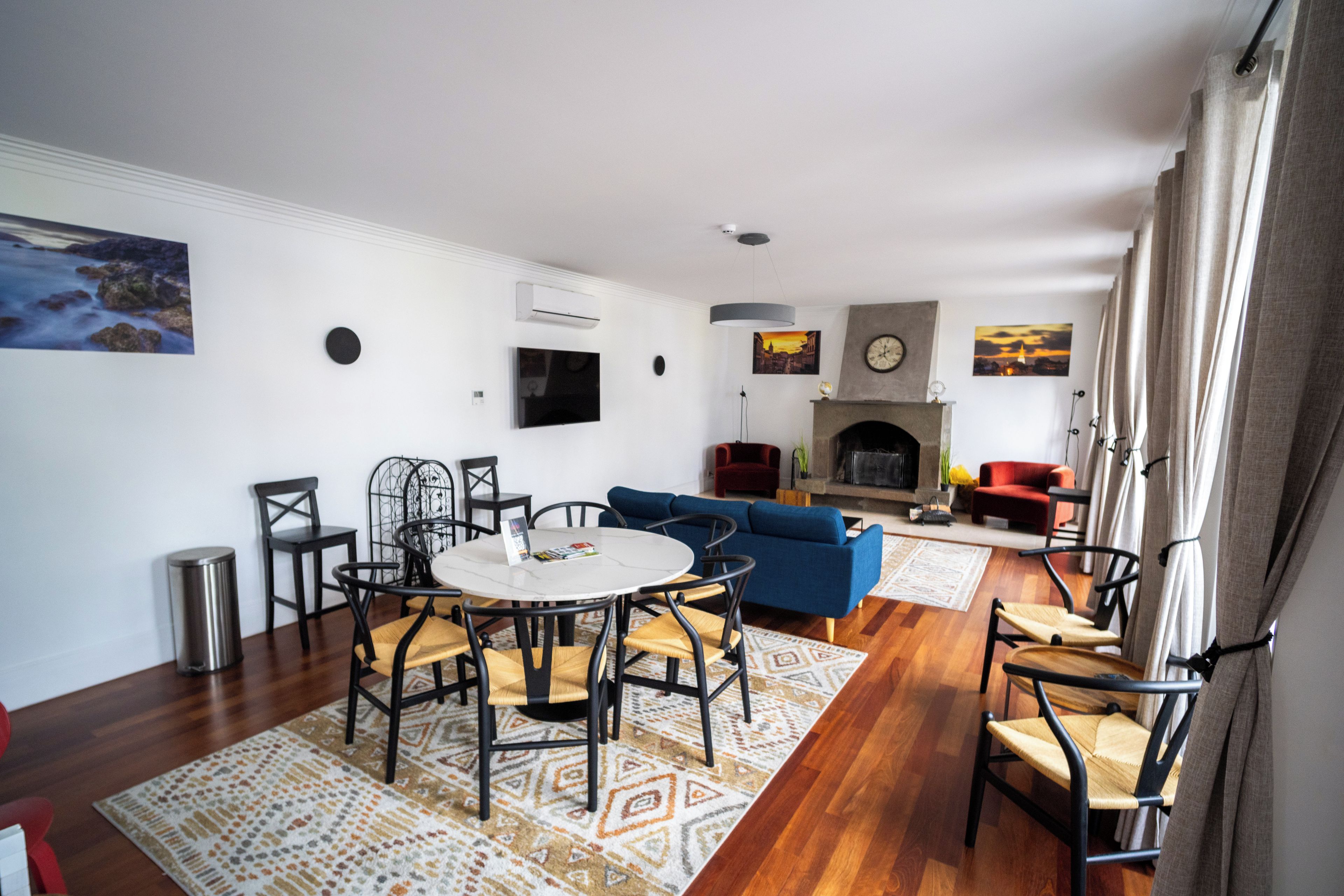 A modern living room with a fireplace, a dining area with a round table and chairs, and a blue sofa.