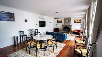 A modern living room with a fireplace, a dining area with a round table and chairs, and a blue sofa.