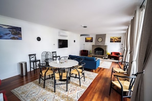 A modern living room with a fireplace, a dining area with a round table and chairs, and a blue sofa. - Aurora Hostel - Suítes e Dormitórios  (Angra do Heroísmo)
