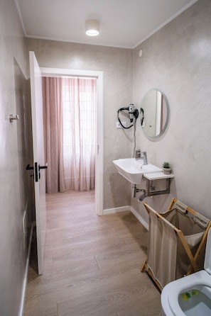 A bathroom with a sink, mirror, and a shower area. - Aurora Hostel - Suítes e Dormitórios  (Angra do Heroísmo)