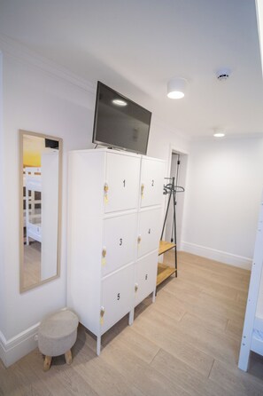 Una habitación con un armario blanco, un televisor sobre él, un taburete pequeño y un espejo en la pared.