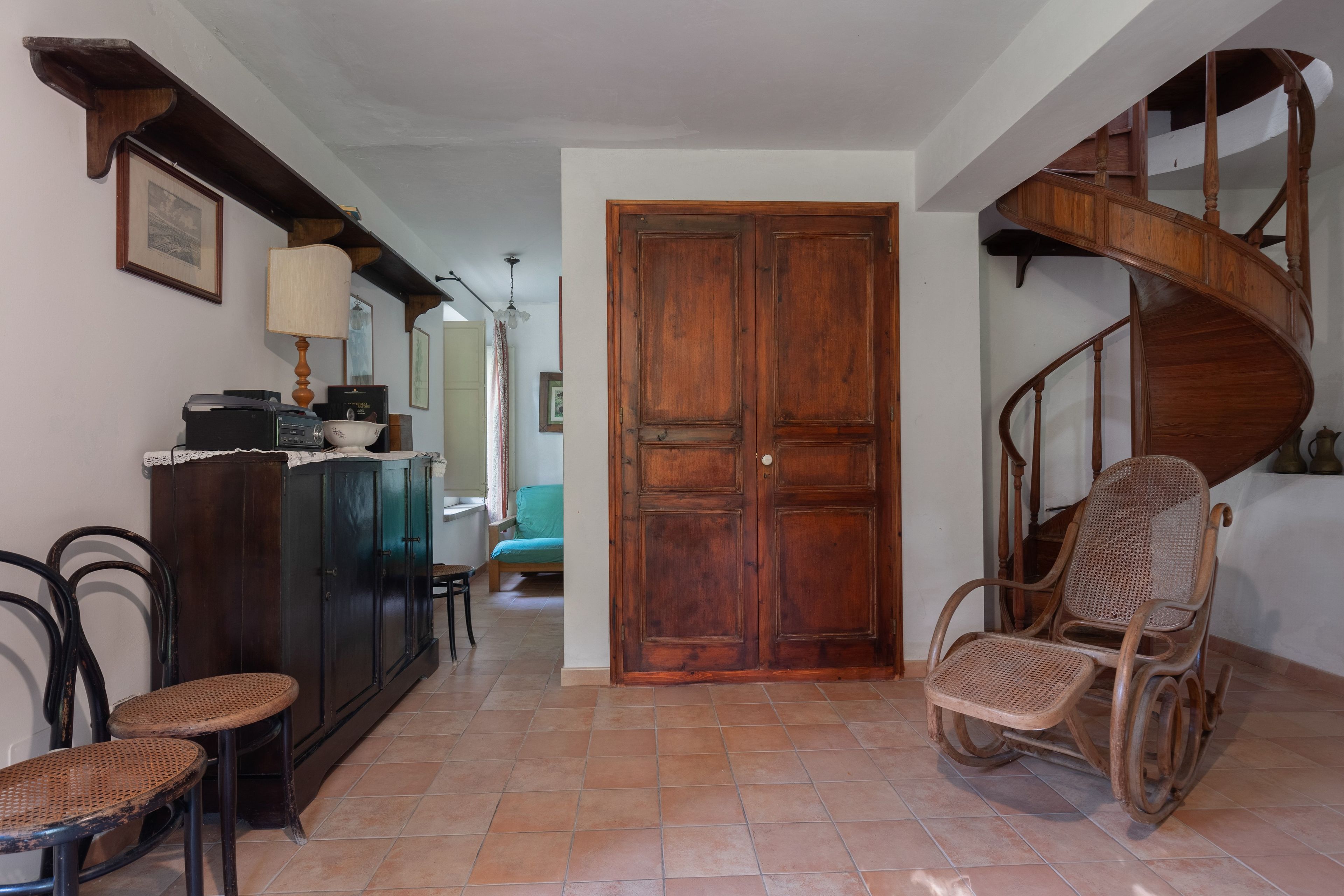 A spacious hallway with a wooden door, a staircase, and a seating area with wicker chairs.