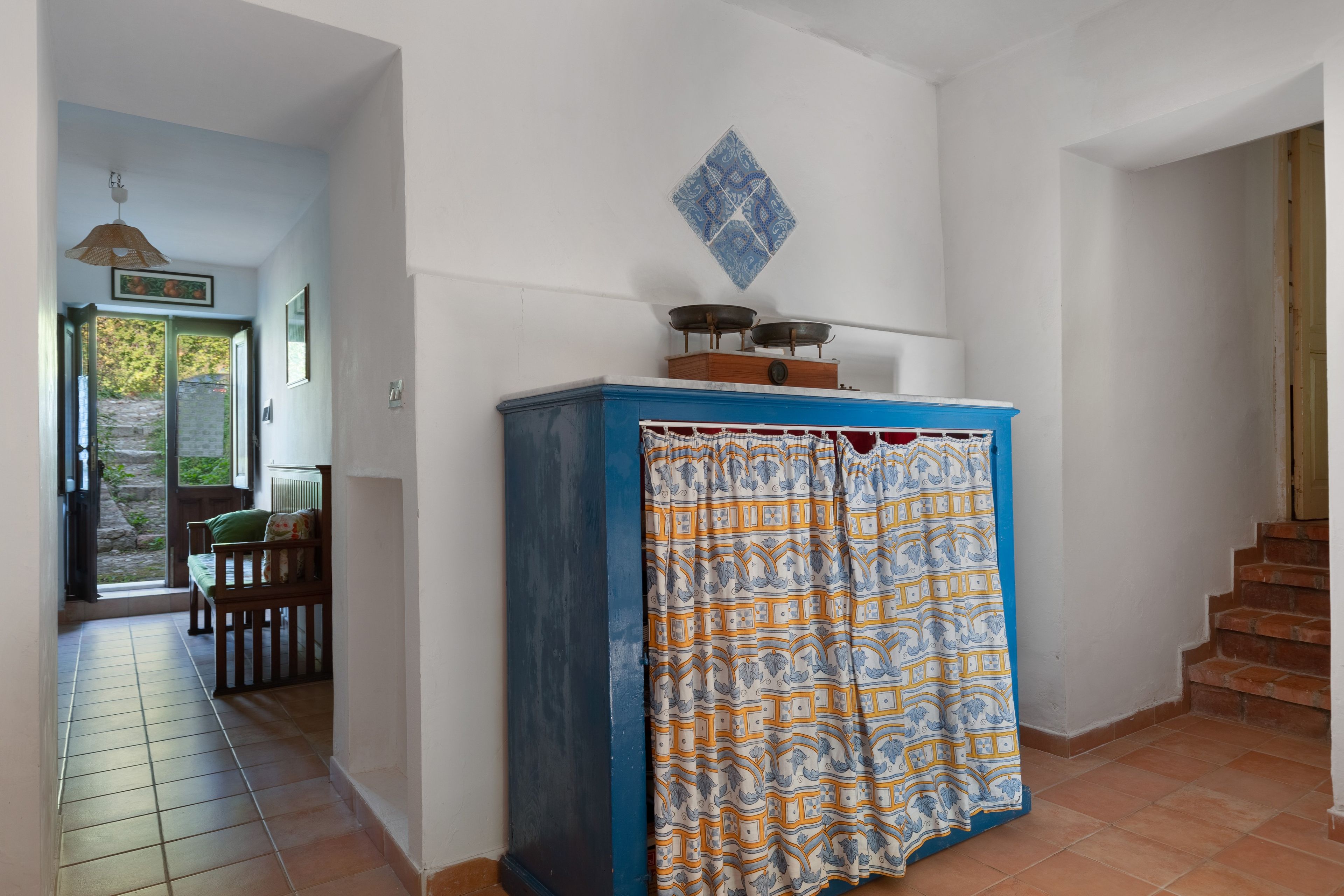 A room with a blue cabinet, a patterned curtain, a staircase, and a door leading outside.