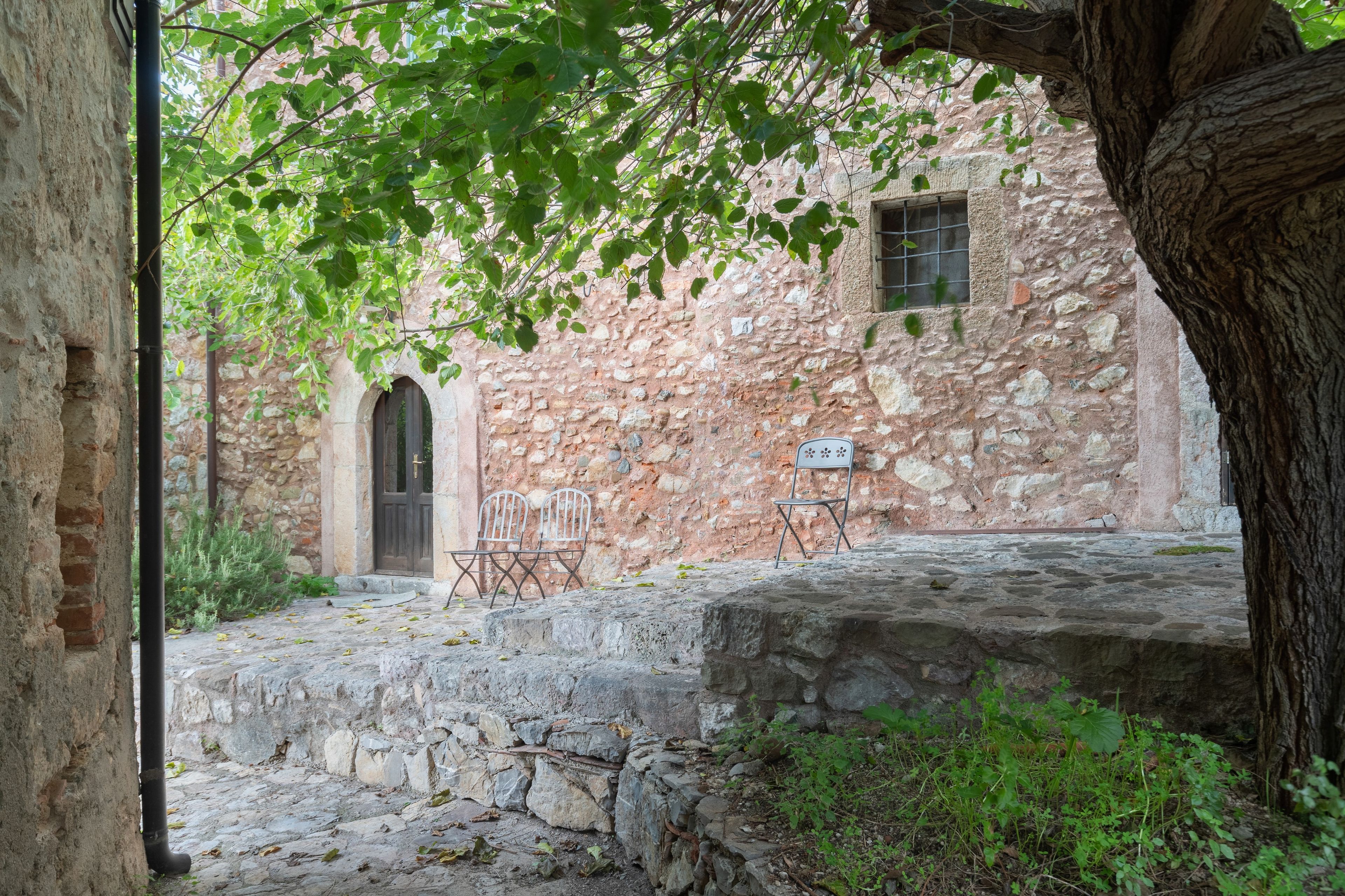 An outdoor courtyard with stone walls, a wooden door, and two metal chairs.