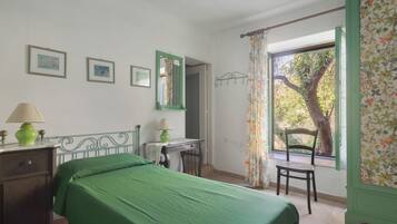 A bedroom with a bed, a chair, a desk, a lamp, and a window with a view of trees.