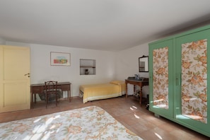 A room with a bed, a desk, a chair, a wardrobe, and a small shelf with a vase.
