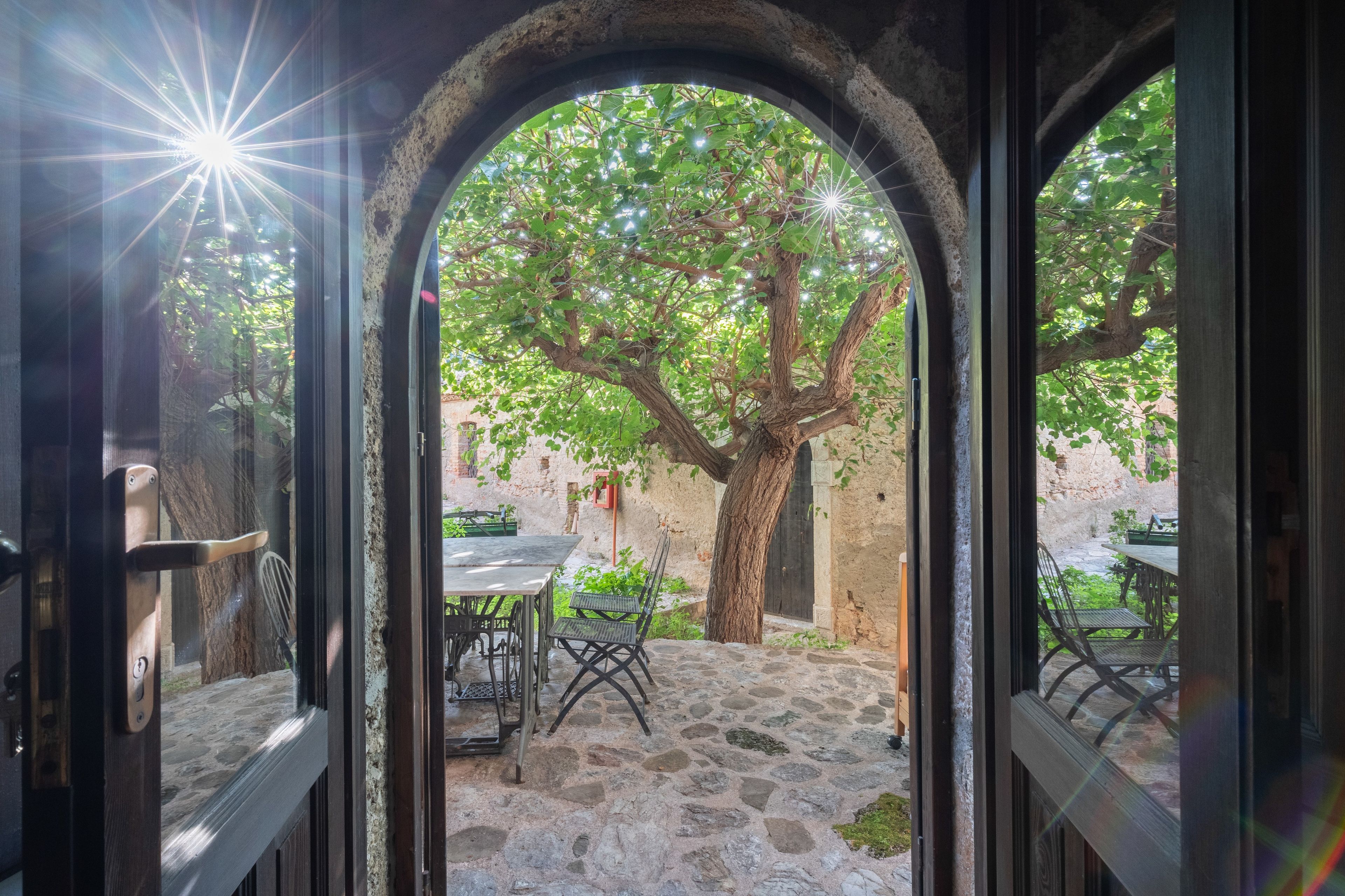 An outdoor patio area with stone flooring, a table, chairs, and a tree.
