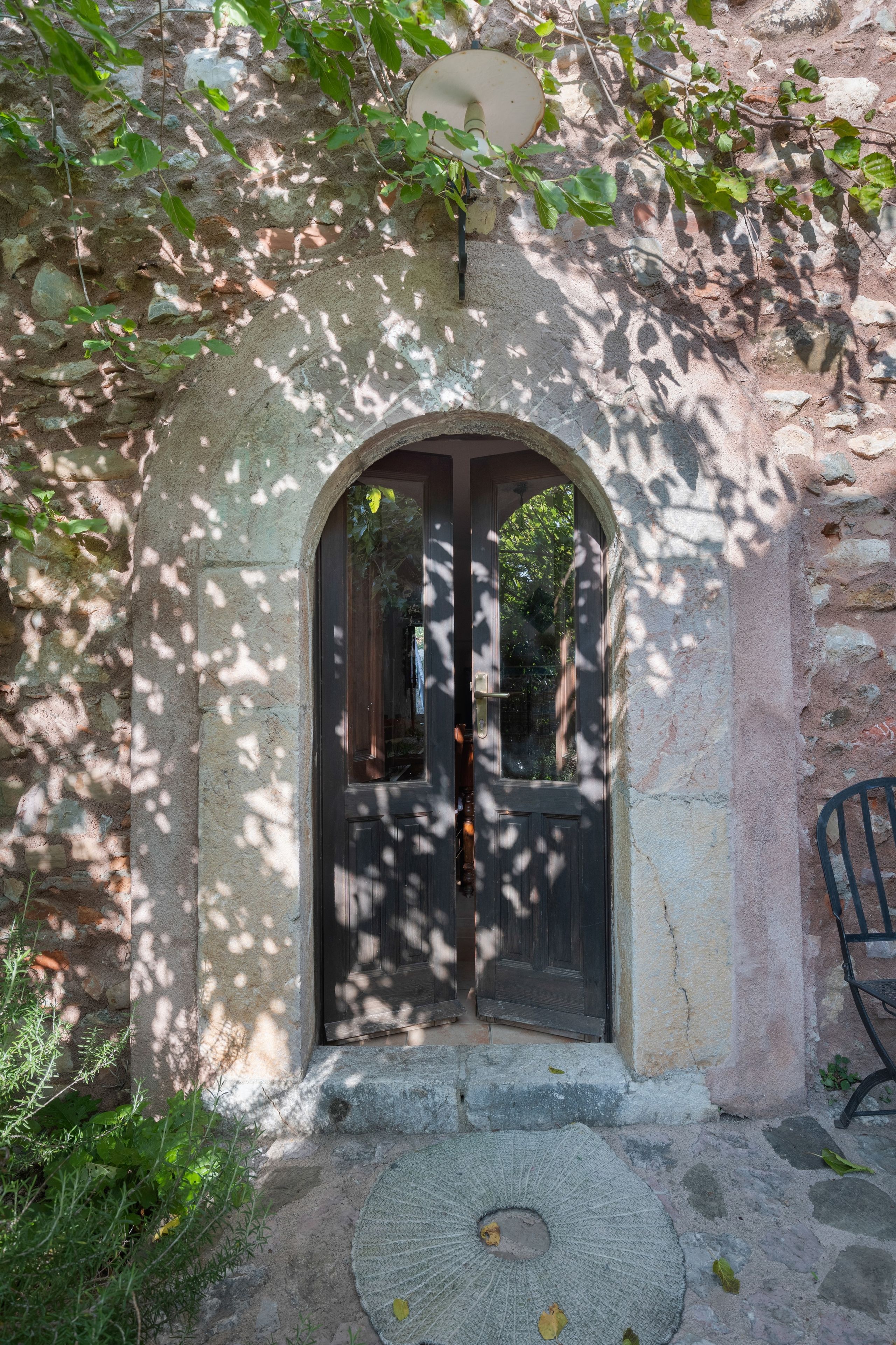 An arched doorway with a dark door, surrounded by stone walls and vegetation.
