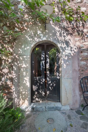An arched doorway with a dark door, surrounded by stone walls and vegetation.