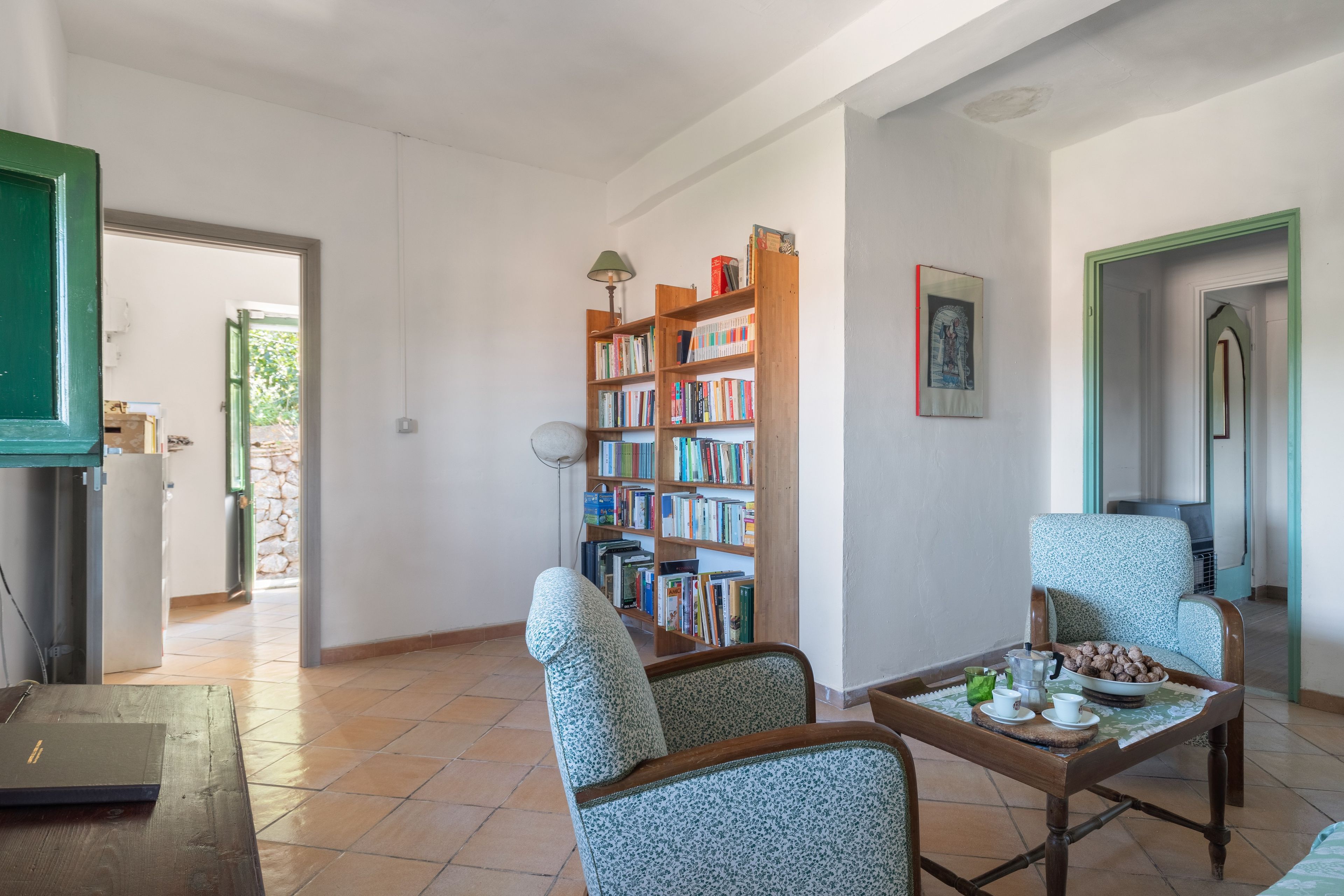Una sala de estar con una estantería, dos sillones estampados, una mesa de centro y una puerta que da a otra habitación.