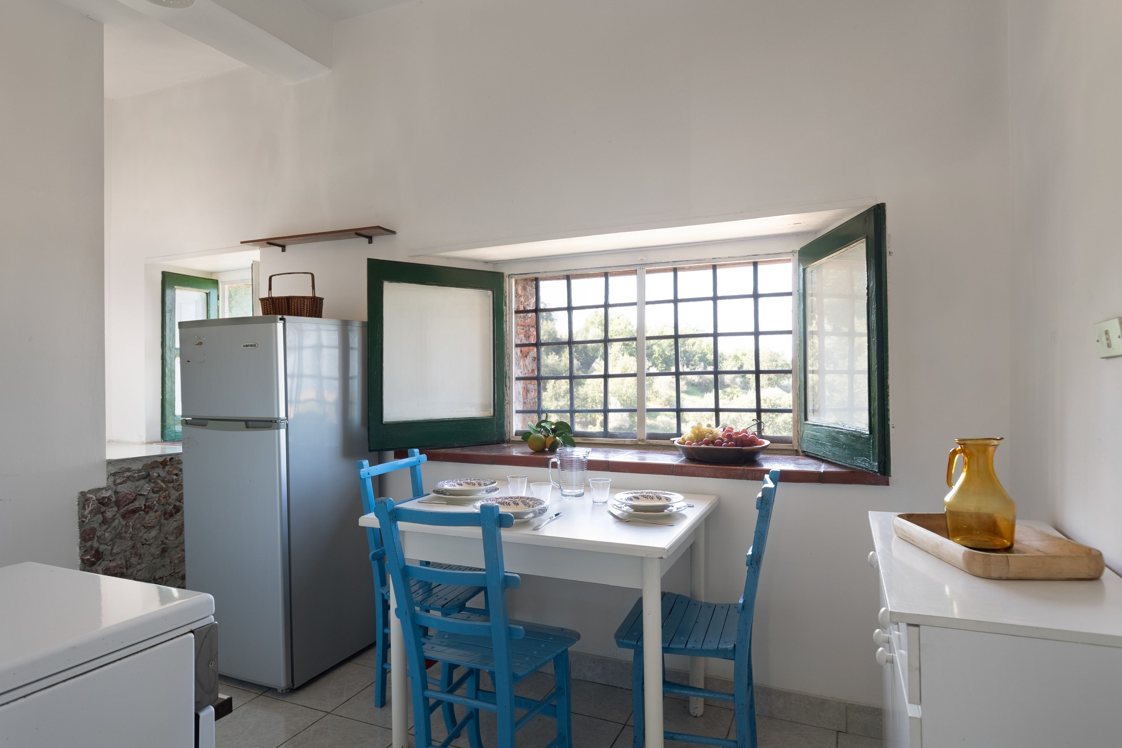 A compact kitchen with a refrigerator, a dining table with chairs, and a window with a view of greenery.