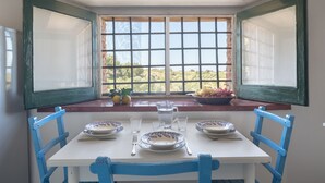 A dining table with blue chairs, a window with a view of greenery, and a bowl of fruit on the windowsill. - Apartment on the oil mill (Torrenova)