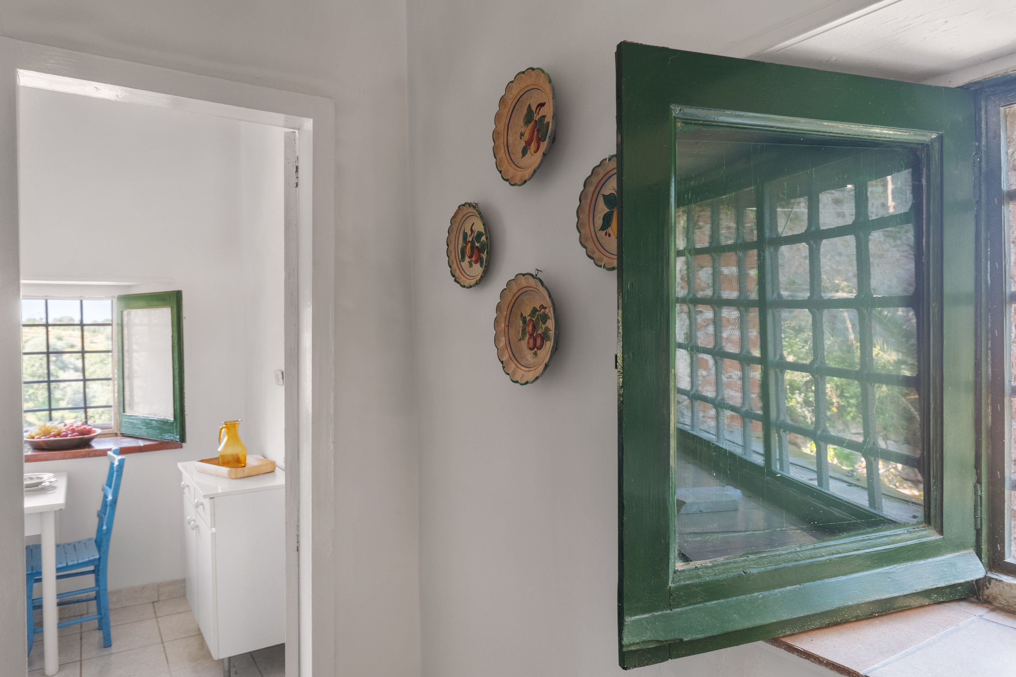 A room with a green-framed window, a white door, and a wall with four decorative plates.