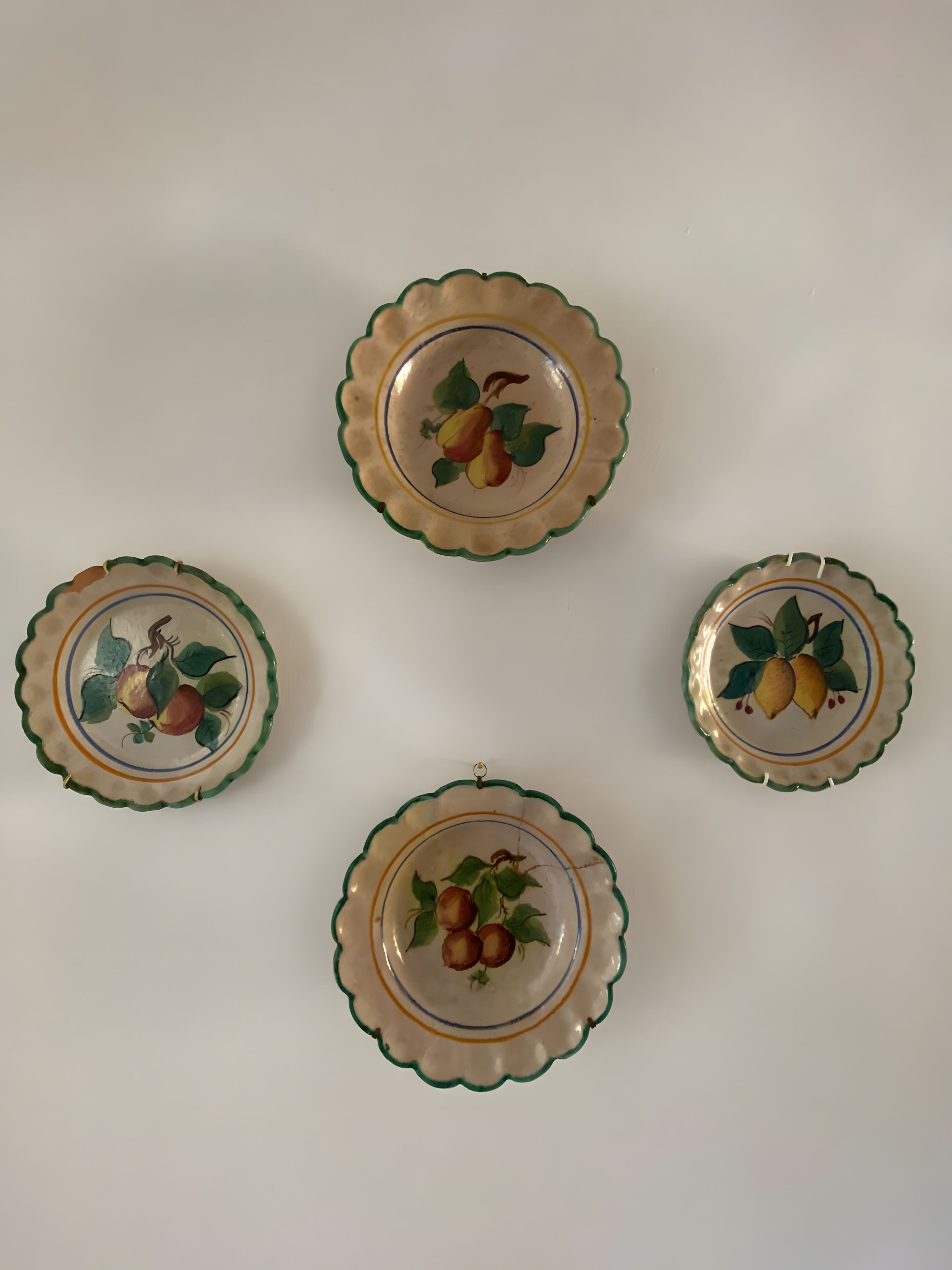Four wall-mounted plates with scalloped edges and fruit designs.