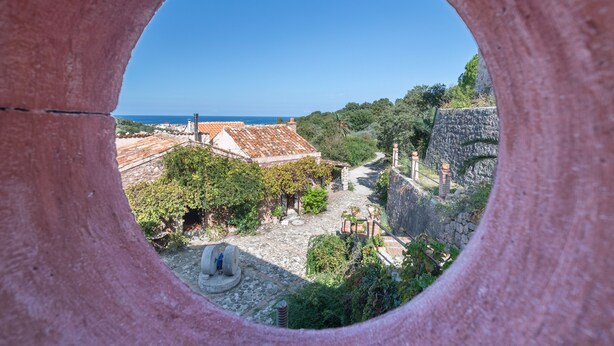 A view through a circular opening of a building with a stone wall, a pathway, and a distant view of the sea. - Apartment on the oil mill (Torrenova)