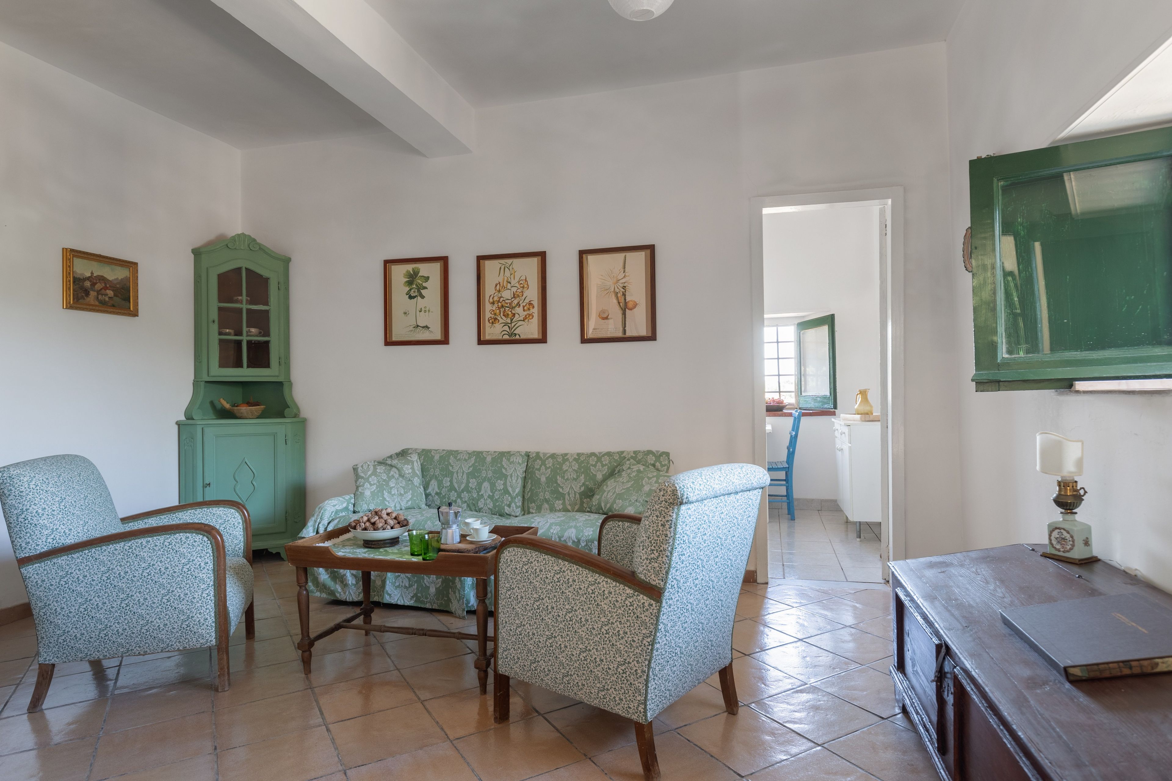 Un salon comprenant un canapé, des fauteuils, un meuble et des reproductions encadrées de motifs botaniques accrochées au mur.