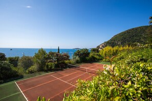 Ein Tennisplatz mit freiem Blick auf das Meer und eine hügelige Landschaft.