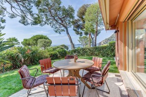 Un patio con tavolo e sedie rotonde, immerso nel verde e con vista sul mare.