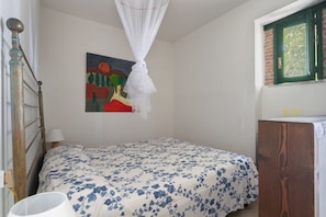 Quarto com cama, pintura, janela e mesa de cabeceira.