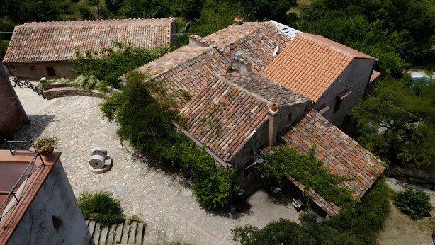 A courtyard with a tiled roof, stone walls, and surrounding greenery. - Azienda Agricola Santo Pietro - Il Frantoio (Torrenova)