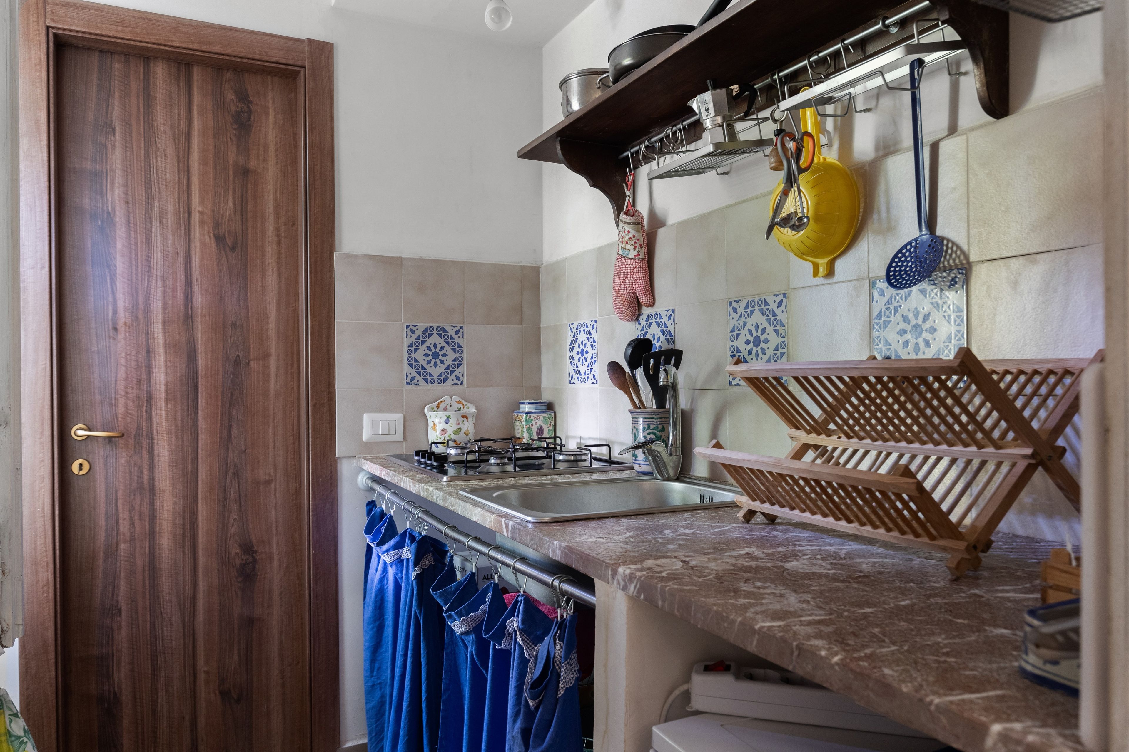A kitchen with a wooden door, tiled backsplash, and a hanging pot rack.