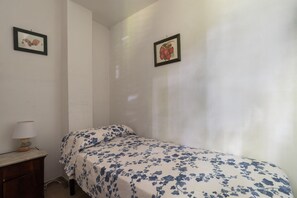 A bedroom with a single bed, a nightstand, a lamp, and two framed pictures on the wall.
