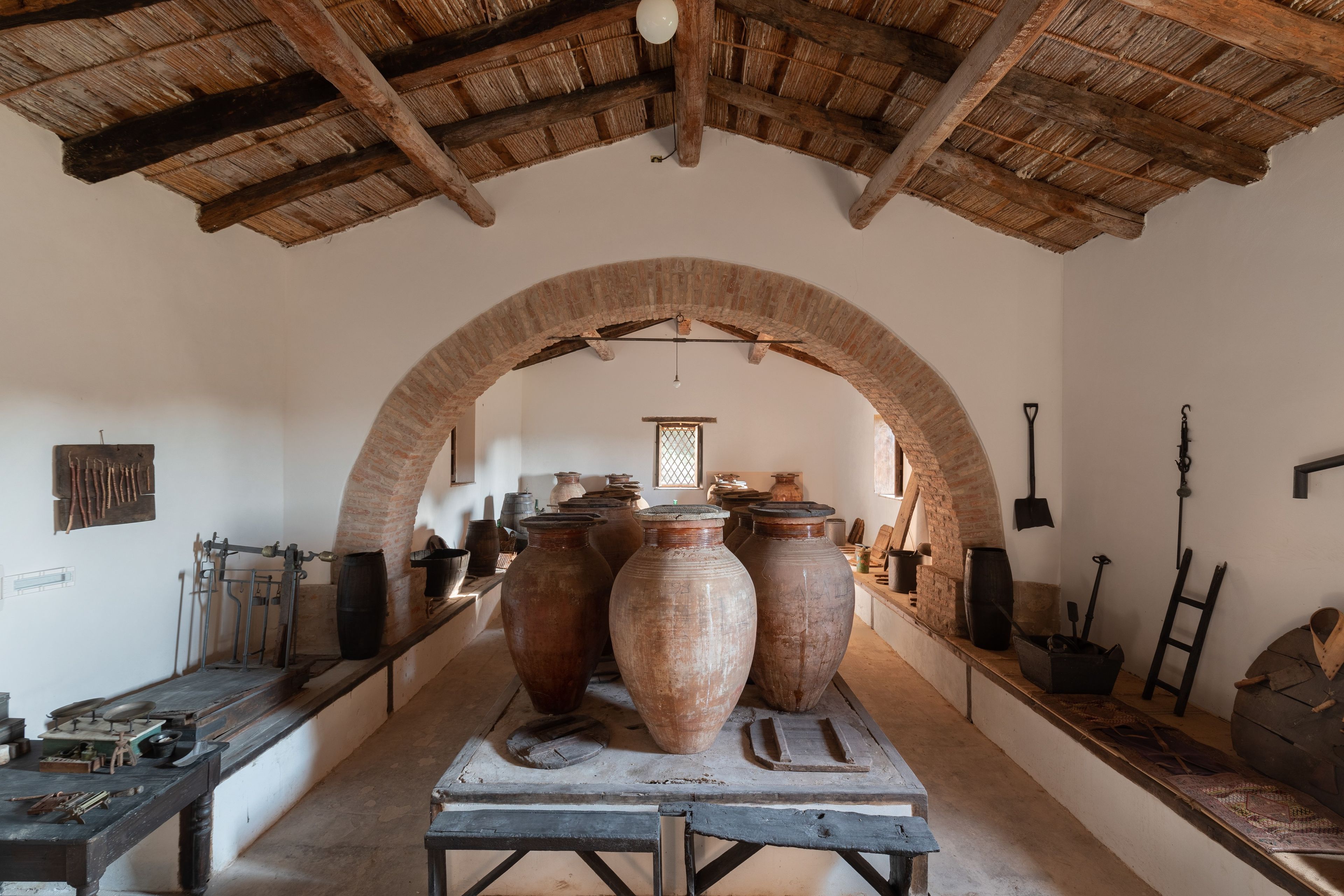 An interior with a vaulted ceiling, large pottery, and traditional tools.
