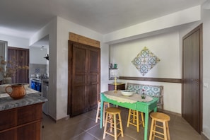 Uma área de refeições com mesa, banquetas, um elemento decorativo na parede e uma porta de madeira.
