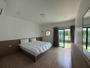A modern bedroom with a large bed, a round mirror, and a sliding glass door leading to a balcony. - Cozy 1-bedroom bungalow in perfect Phuket with AC included (Phuket)