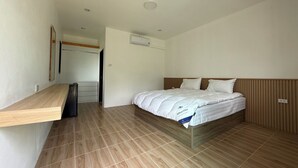 Habitación de hotel con cama, cabecera de madera, banco integrado, escritorio pequeño y puerta que conduce a otra habitación.
