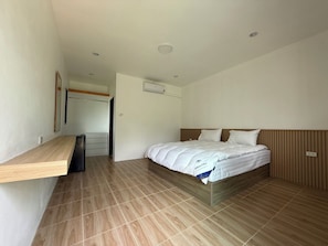 A hotel room with a bed, a wooden headboard, a built-in bench, a small desk, and a door leading to another room. - Cozy 1-bedroom bungalow in perfect Phuket with AC included (Phuket)