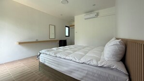 Un dormitorio con cama, suelo de madera, pared blanca e iluminación empotrada en el techo.
