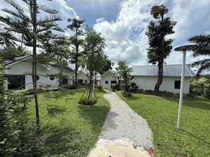 A pathway leading to a row of white buildings with a gravel path and lush greenery. - Cozy 1-bedroom bungalow in perfect Phuket with AC included (Phuket)