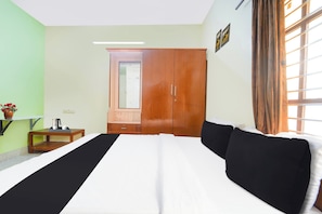 Quarto de hotel com cama, guarda-roupa, uma pequena mesa com um vaso de flores e uma janela com cortinas.