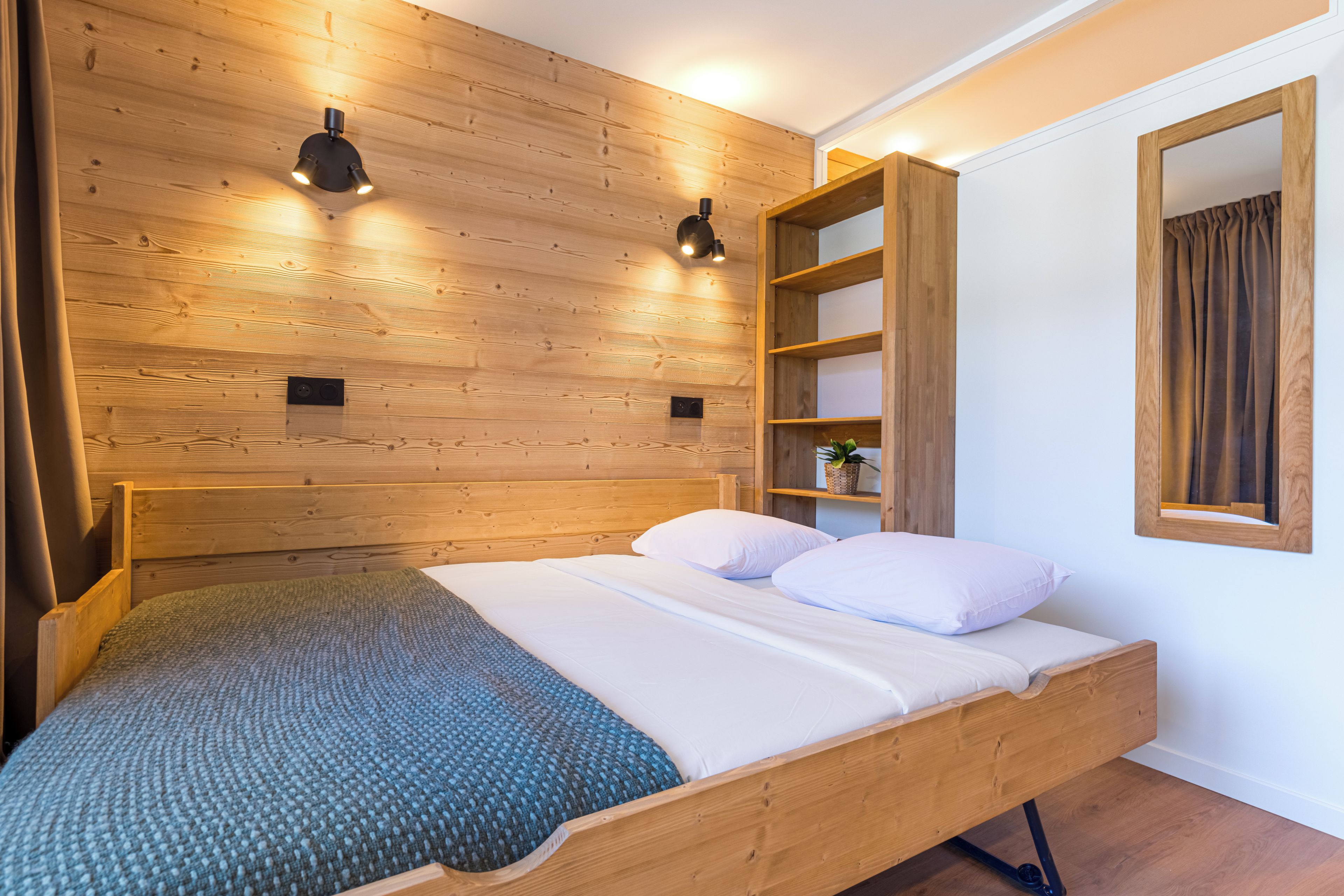 A wooden bed with a headboard, a bedside shelf, and a wall-mounted light fixture.