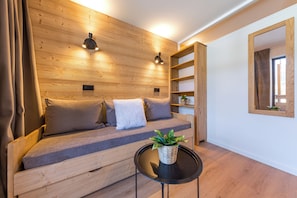 A wooden wall with built-in lighting, a sofa with cushions, a small table with a plant, and a mirror on the wall. - “V21” by Versant Collection (Val Thorens)