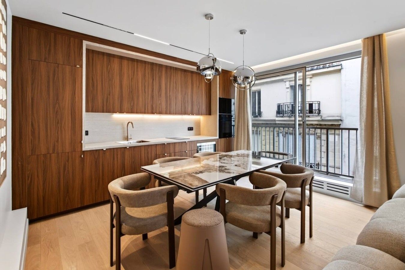 A modern kitchen with wooden cabinetry, a dining table with chairs, and a balcony with a view.