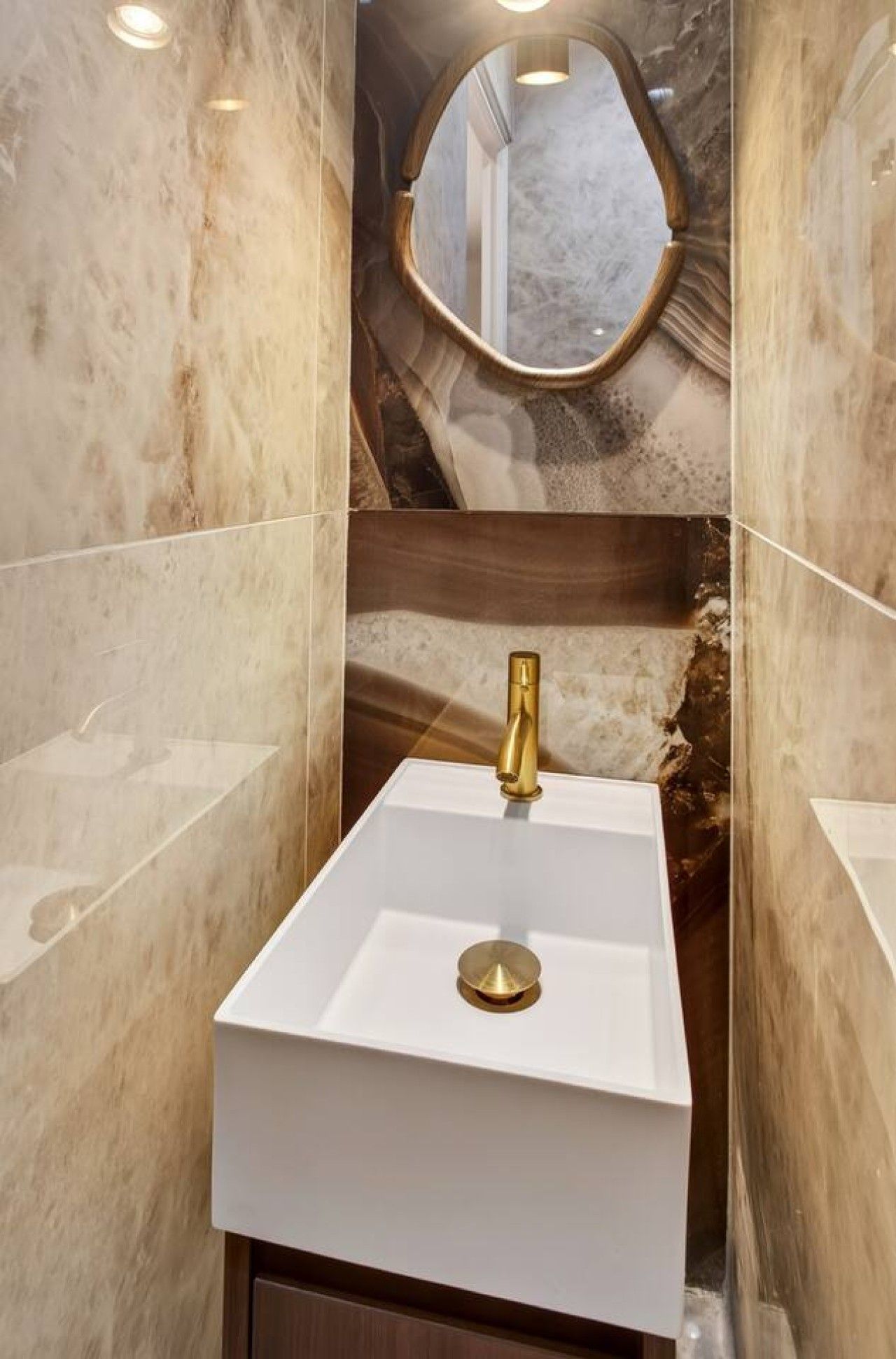 A bathroom with a white sink, gold faucet, and marble walls.