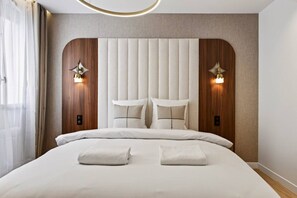 Ein modernes Hotelzimmer mit einem großen Bett, einer Kopfteil mit vertikalen Paneelen und Wandleuchten.