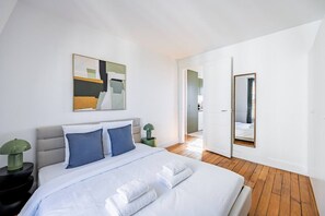 Ein Schlafzimmer mit einem Bett, einem Nachttisch, einer Lampe, einem Gemälde, einem Spiegel und einem Holzboden.