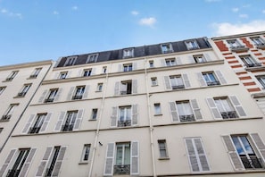 A multi-story building with white facades and shutters, featuring balconies with black railings. - Flexible Lease – Modern – 1 Bedroom – Parisian Charm (Levallois-Perret)