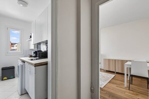 A modern kitchen with white cabinets, a black countertop, and a window. - Flexible Lease – Modern – 1 Bedroom – Parisian Charm (Levallois-Perret)