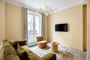 A modern living room with a sofa, a round coffee table, a chair, a TV mounted on the wall, and a large window with curtains. - Rome - Premium - Parc Monceau - Villiers - 5-Bedroom - Haussmann Style (Paris)