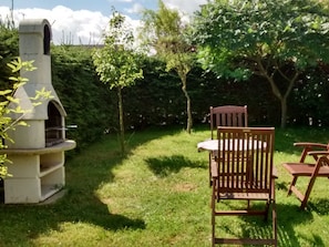Un espacio al aire libre con una parrilla de piedra, rodeado de césped y árboles.