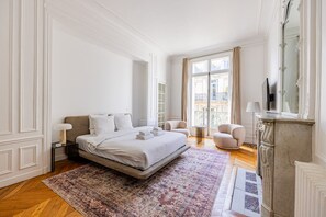 A spacious bedroom with a large bed, a sitting area with chairs, a fireplace, and a balcony with a view. - Parc Monceau - Arc de Triomphe - 5-bedroom - Premium (Paris)