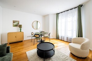 Ein modernes Wohnzimmer mit einem runden Esstisch, einer Couch, einem Schrank und einem großen Fenster mit Vorhängen.