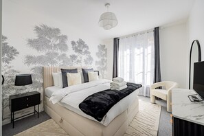 Een moderne slaapkamer met een bed, nachtkastje, lamp, stoel en een televisie.