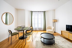 Ein modernes Wohnzimmer mit einem runden Esstisch, Stühlen, einer Couch, einem Fernseher und einer Lampe.