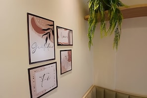 A wall with four framed artworks, a hanging fern, and a cushioned bench.